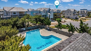A residential area with a swimming pool, houses with balconies, and a clear blue sky. - Seven Sisters 26: Oceanside, hot tub, community pool, easy beach access. (Nags Head)