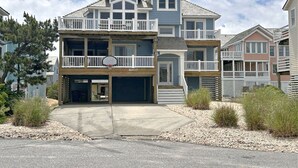 A multi-story residential building with a two-story balcony, a garage, and a clear driveway. - Seven Sisters 26: Oceanside, hot tub, community pool, easy beach access. (Nags Head)