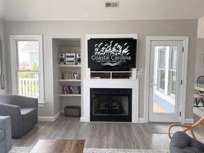 Ein Wohnzimmer mit Kamin, einem darüber angebrachten Fernseher und einem Bücherregal.