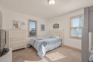 A bedroom with a bed, dresser, and a window with blinds. - Seven Sisters 26: Oceanside, hot tub, community pool, easy beach access. (Nags Head)