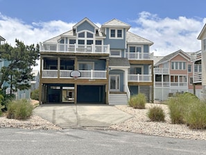 A two-story residential building with a garage, a balcony on the second floor, and a clear sky.