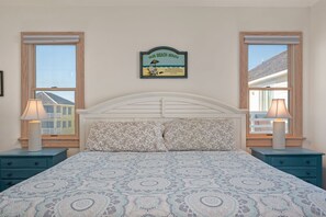 A bedroom with a bed, two nightstands, a wall sign, and windows.
