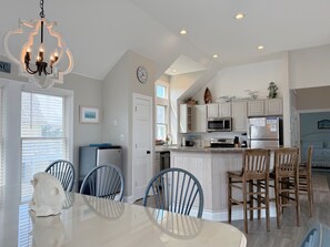 A modern kitchen with white cabinetry, a central island, and a dining area with a white table and blue chairs.