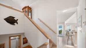 A staircase with wooden handrails, a fish decoration on the wall, and a kitchen area with bar stools. - Seven Sisters 26: Oceanside, hot tub, community pool, easy beach access. (Nags Head)