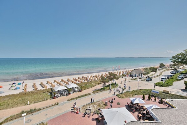 Un complexe hôtelier en bord de mer, avec des rangées de chaises longues, une promenade dallée et des parasols de plage.