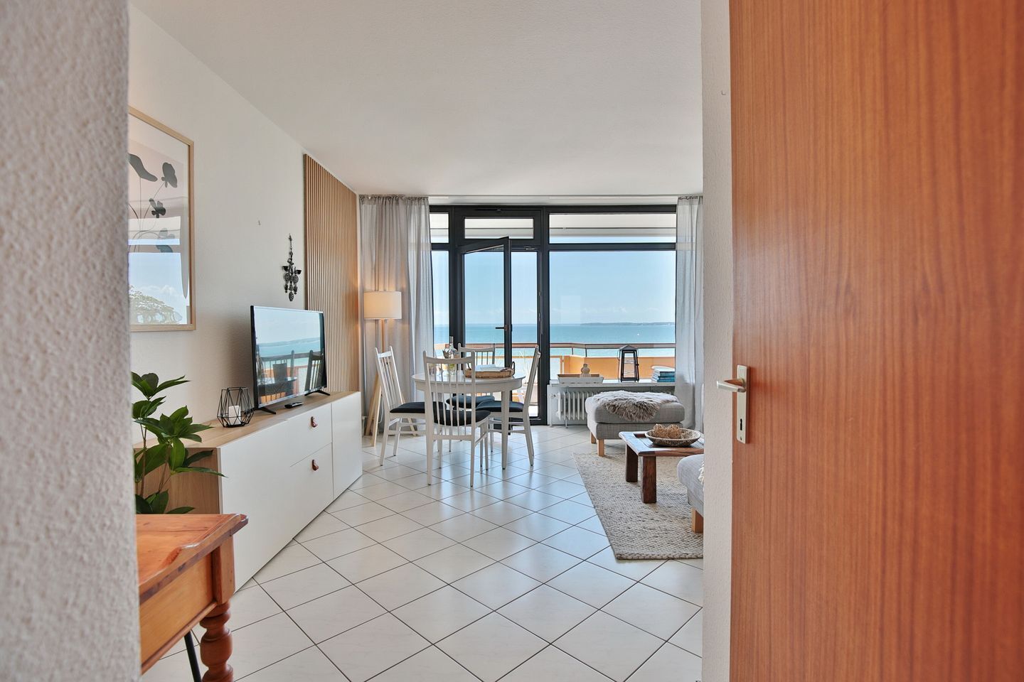 A modern hotel room with a balcony, a dining area, and a TV.