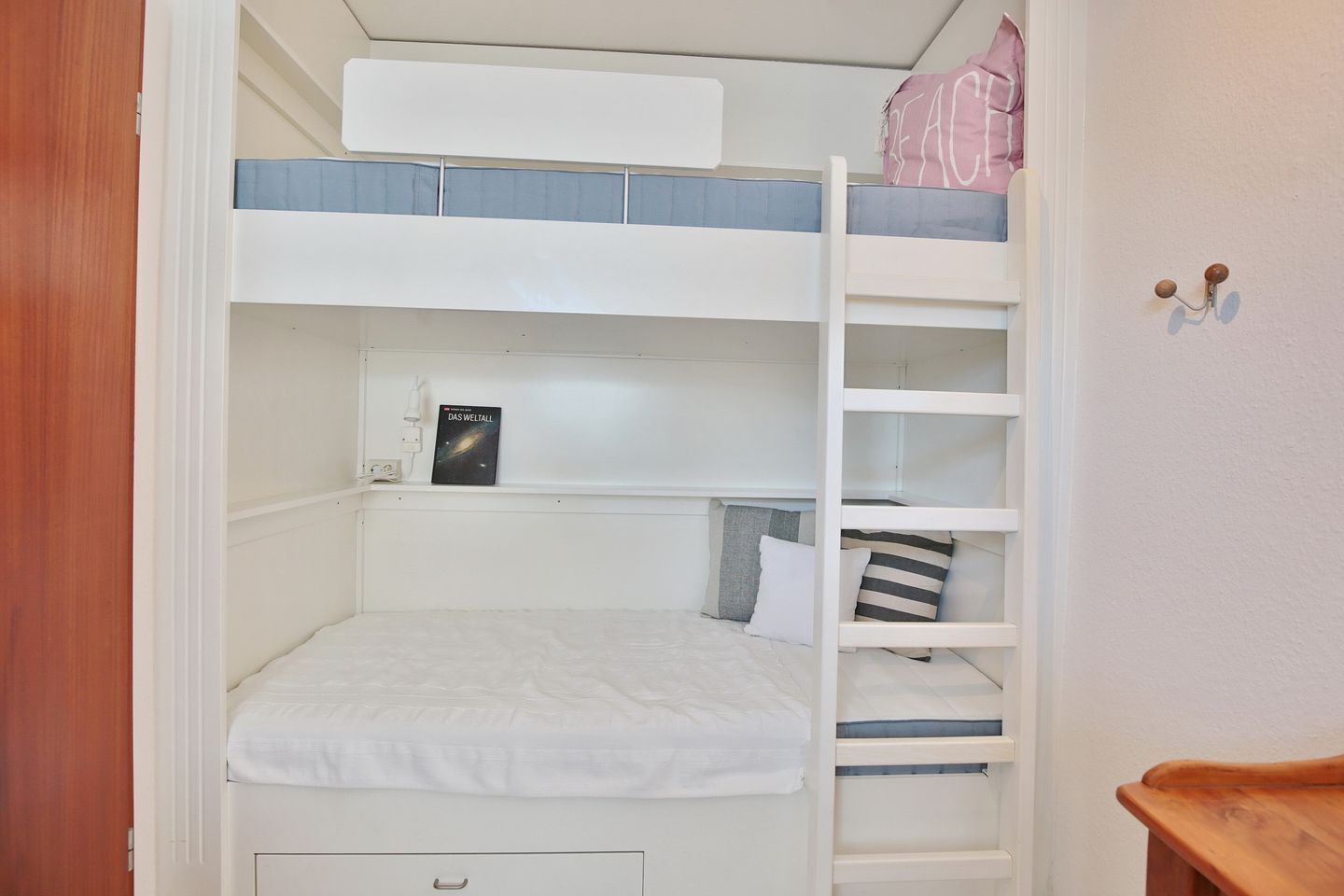 A bunk bed room with a ladder, a small desk, and a wall-mounted shelf.
