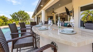 Un área de comedor al aire libre con piscina, sillas de mimbre y una barra.