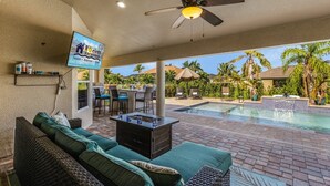 Un espacio exterior techado con piscina, un sofá, un televisor y una zona de bar.