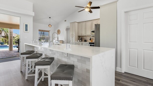 Una cocina moderna con una isla grande, armarios blancos y un ventilador de techo.