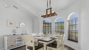 Un comedor con una mesa de madera dispuesta para cuatro personas, paredes blancas y un ventilador de techo.