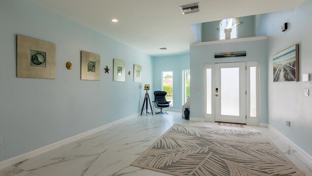 A spacious hallway with light blue walls, a marble floor, and a large decorative rug. - Lovely water direct home with long water views. (Marco Island)