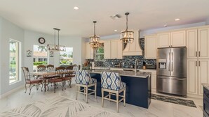 A spacious kitchen with a central island, pendant lights, and a large refrigerator. - Lovely water direct home with long water views. (Marco Island)