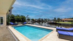 A rectangular pool with clear blue water, surrounded by lounge chairs and a covered seating area. - Lovely water direct home with long water views. (Marco Island)