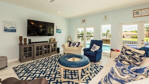 A living room with a TV, sofa, armchair, and a view of a pool. - Lovely water direct home with long water views. (Marco Island)