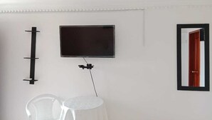 Una habitación con una televisión montada, un estante en la pared, una mesa redonda y un espejo que refleja una puerta.