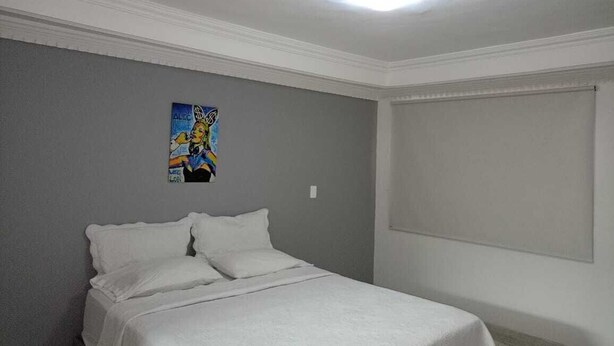 Un dormitorio con cama, una lámpara en el techo, una ventana con persianas y una pared con un cuadro de colores.