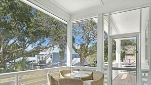 A covered outdoor area with a wooden deck, wicker furniture, and a glass door leading to an outdoor space.