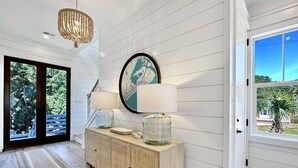 A hallway with a wooden floor, a woven bench, a large wall map, and a door leading outside.