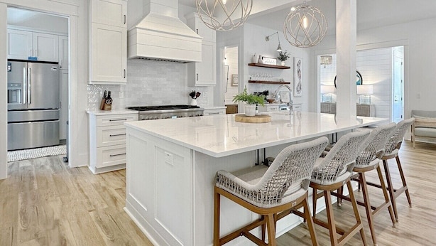 A modern kitchen with white cabinetry, a large island with bar stools, and pendant lighting.