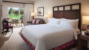 Une chambre d’hôtel dotée d’un grand lit, d’un bureau avec une chaise, d’un canapé et offrant une vue sur un terrain de golf grâce à une porte coulissante.