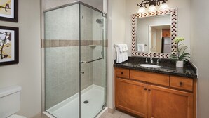 Une salle de bain dotée d’une douche à parois de verre, d’un lavabo avec un plan de travail en marbre, de meubles en bois et d’un miroir orné d’un cadre décoratif.
