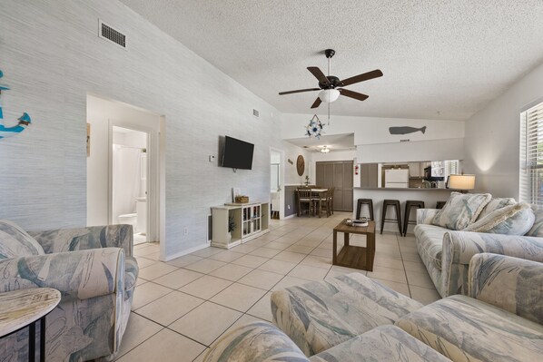 A spacious living area with a ceiling fan, a kitchen in the background, and a dining area.