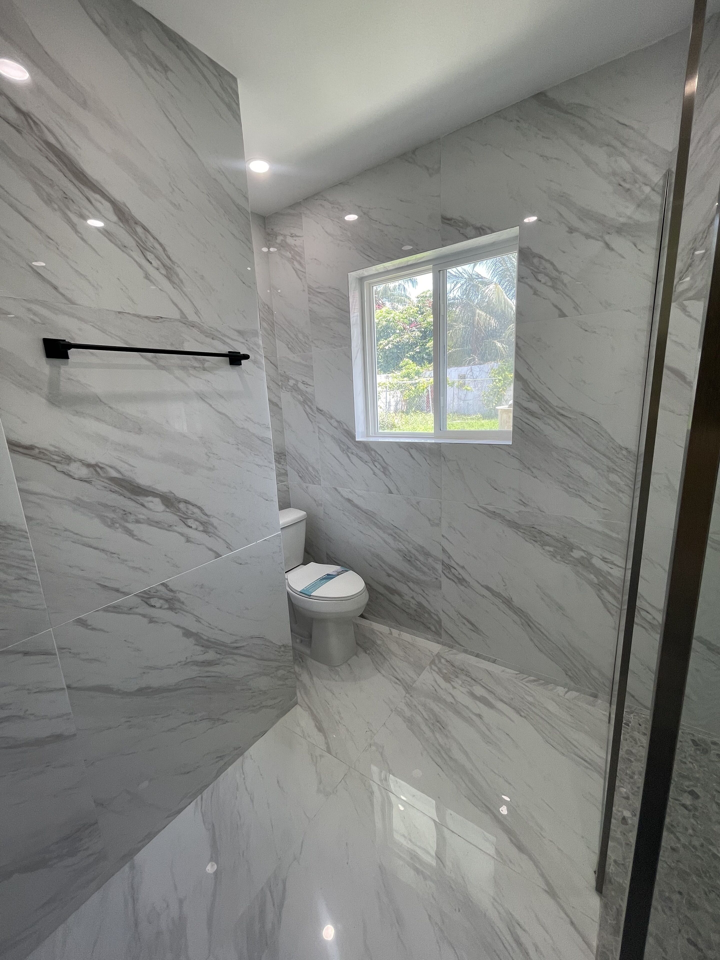 A bathroom with a toilet, a shower area, and a window providing natural light.