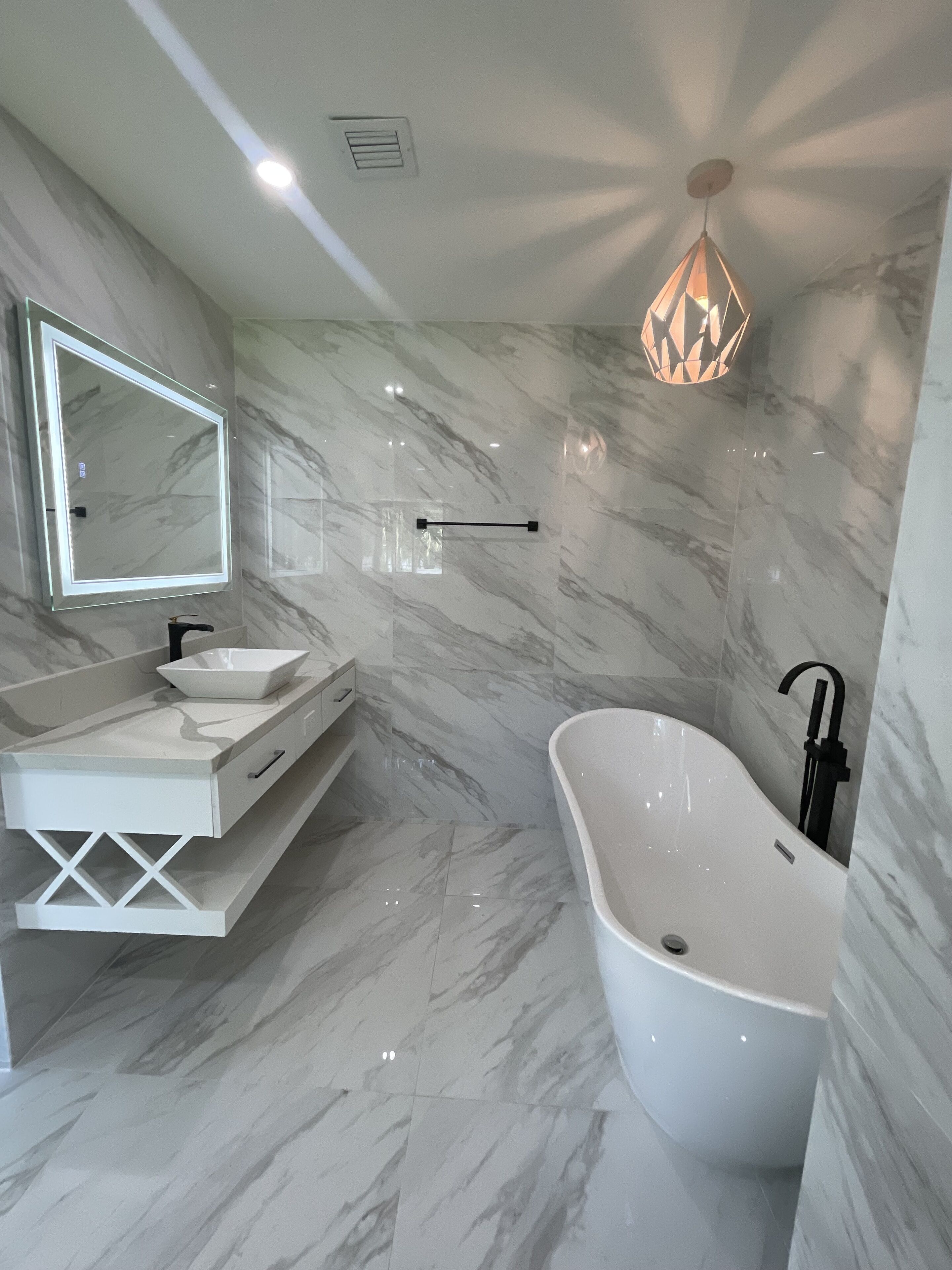 Un baño moderno con una bañera independiente, un espejo grande y una lámpara colgante.