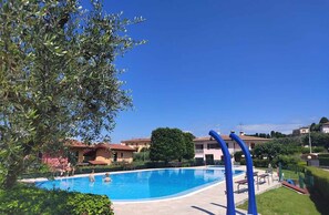 Una piscina con un cielo azul despejado, rodeada de vegetación y edificios residenciales.
