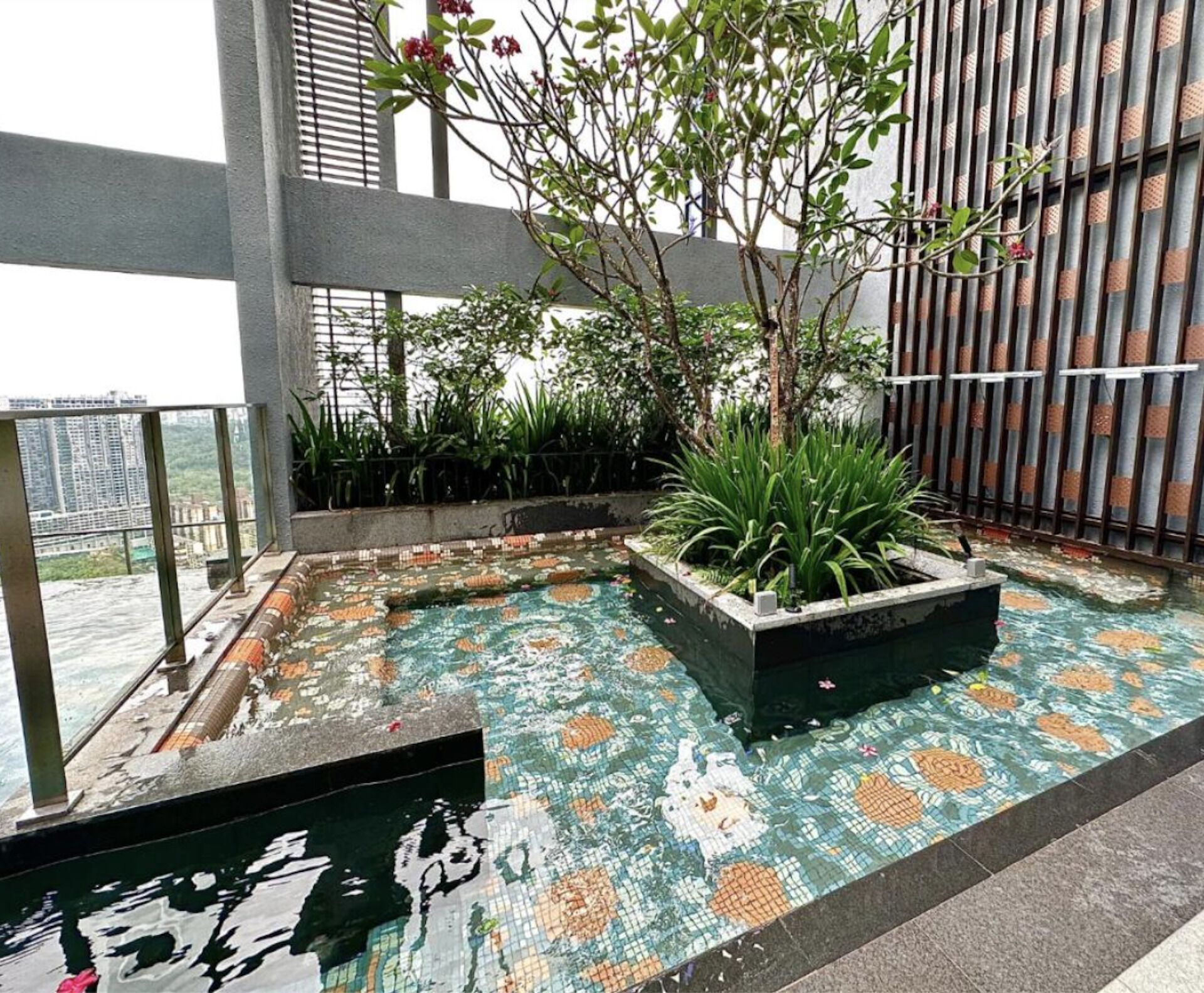 Un jardín en la azotea con una piscina pequeña, rodeado de plantas en macetas y una valla de bambú.