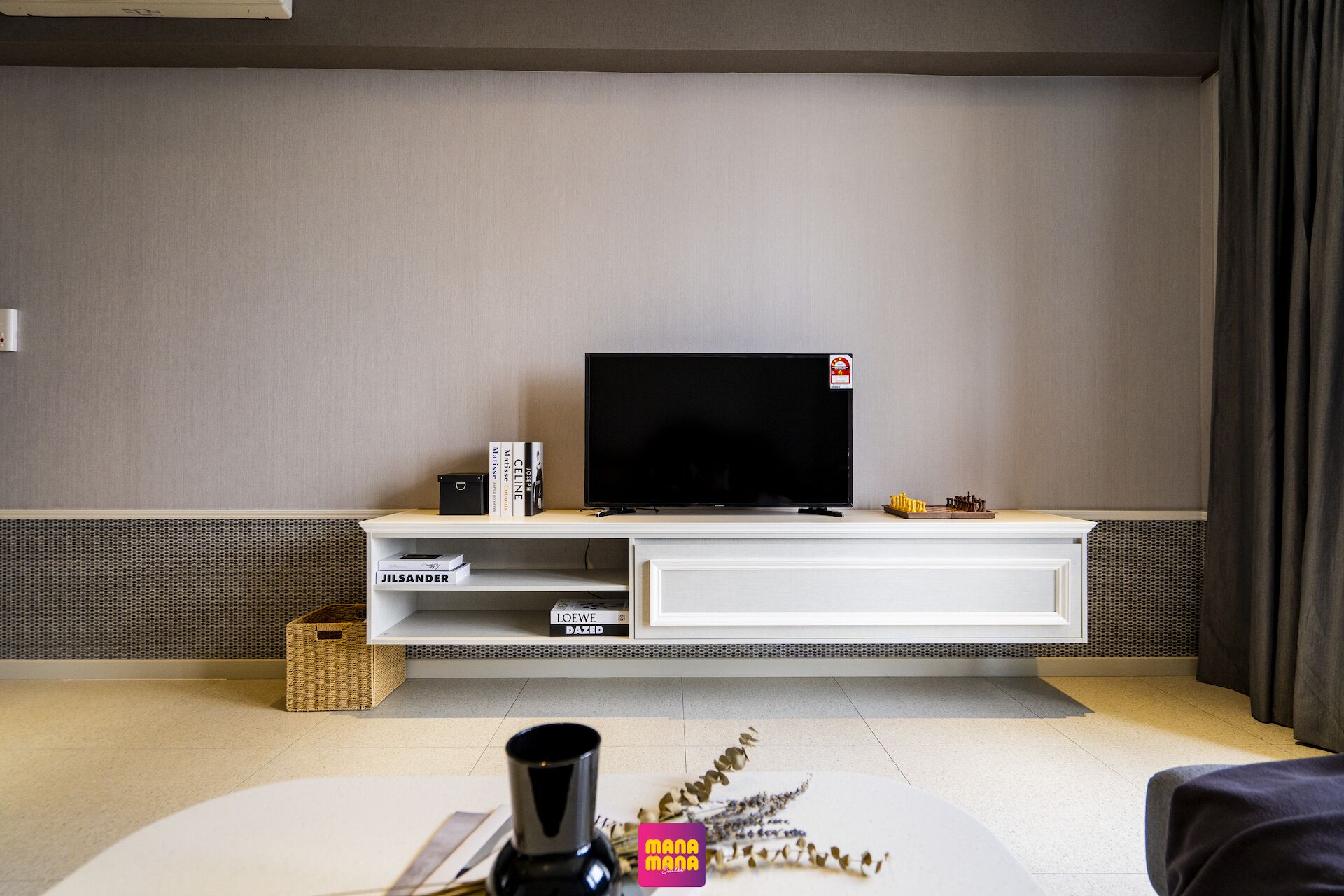Un salon moderne avec un téléviseur à écran plat posé sur un meuble blanc, un petit jeu d’échecs et un vase décoratif sur le sol.