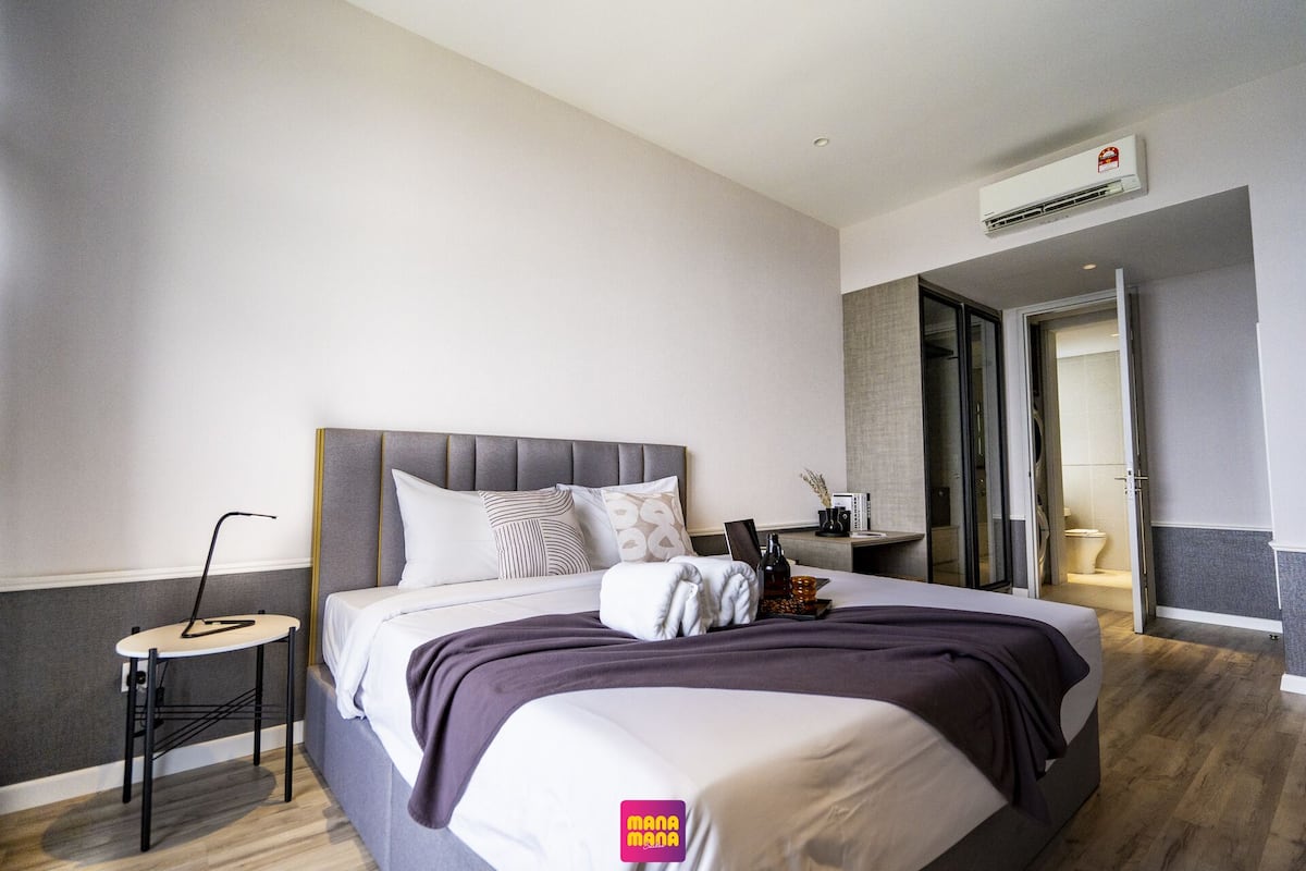 Habitación de hotel moderna con una cama grande, una mesita de noche y un baño visible a través de una puerta abierta.