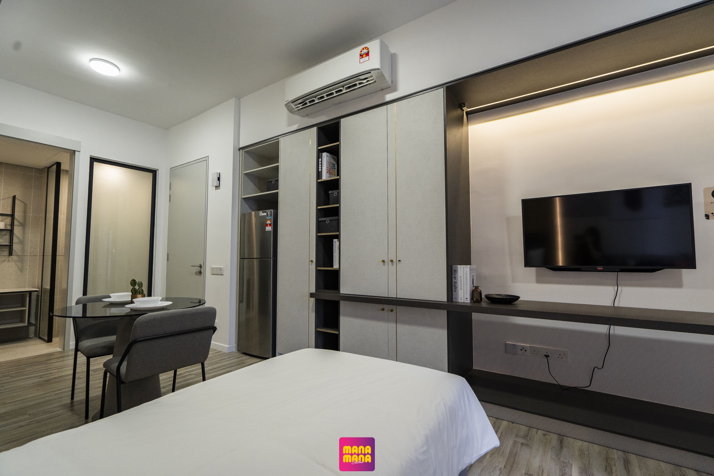 Une chambre d’hôtel moderne équipée d’un lit, d’un bureau avec des chaises, d’une armoire et d’un téléviseur fixé au mur.