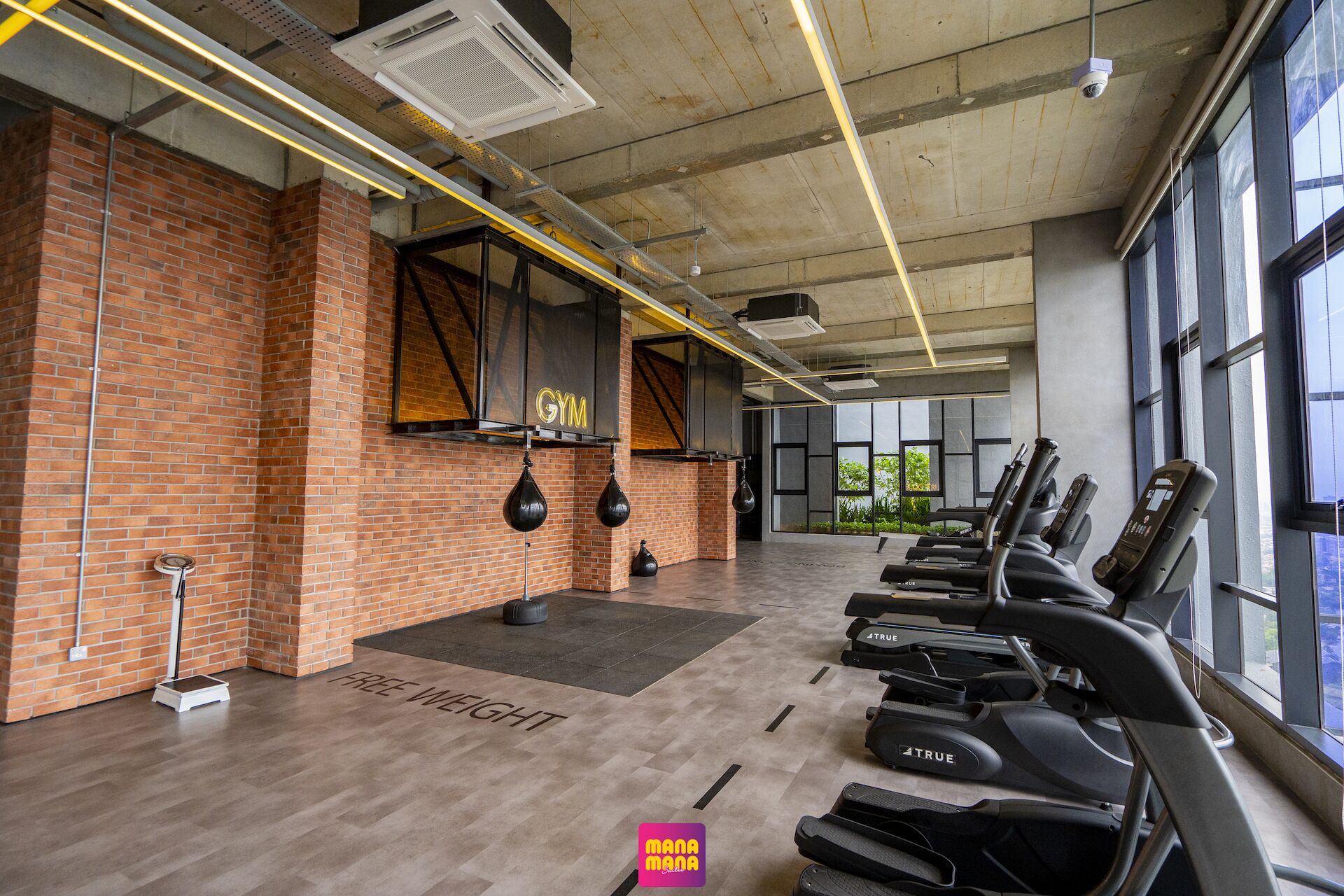 Un gimnasio con paredes de ladrillo, zona de pesas libres, cintas de correr y ventanas amplias.