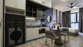 A modern hotel room with a dining area, kitchenette, and a bed.
