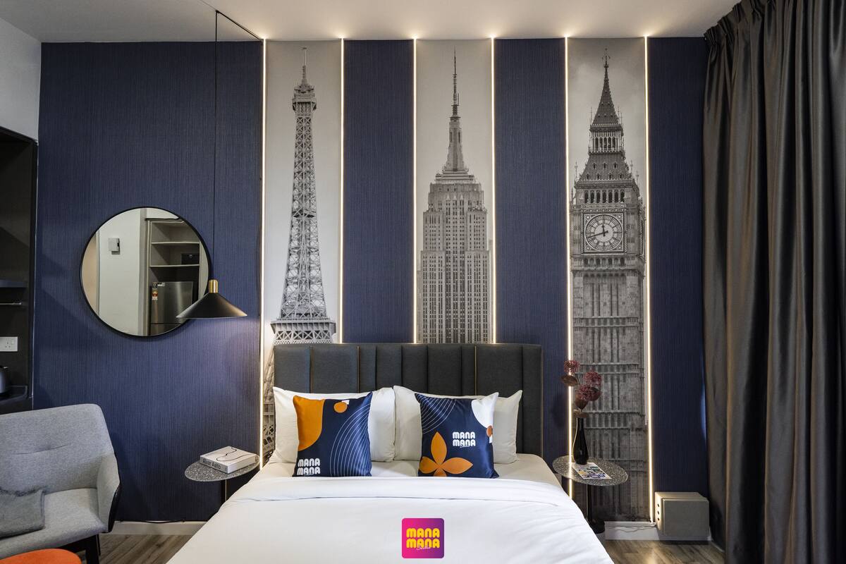 Habitación de hotel con cama, un espejo redondo, una silla y una mesita de noche con lámpara.