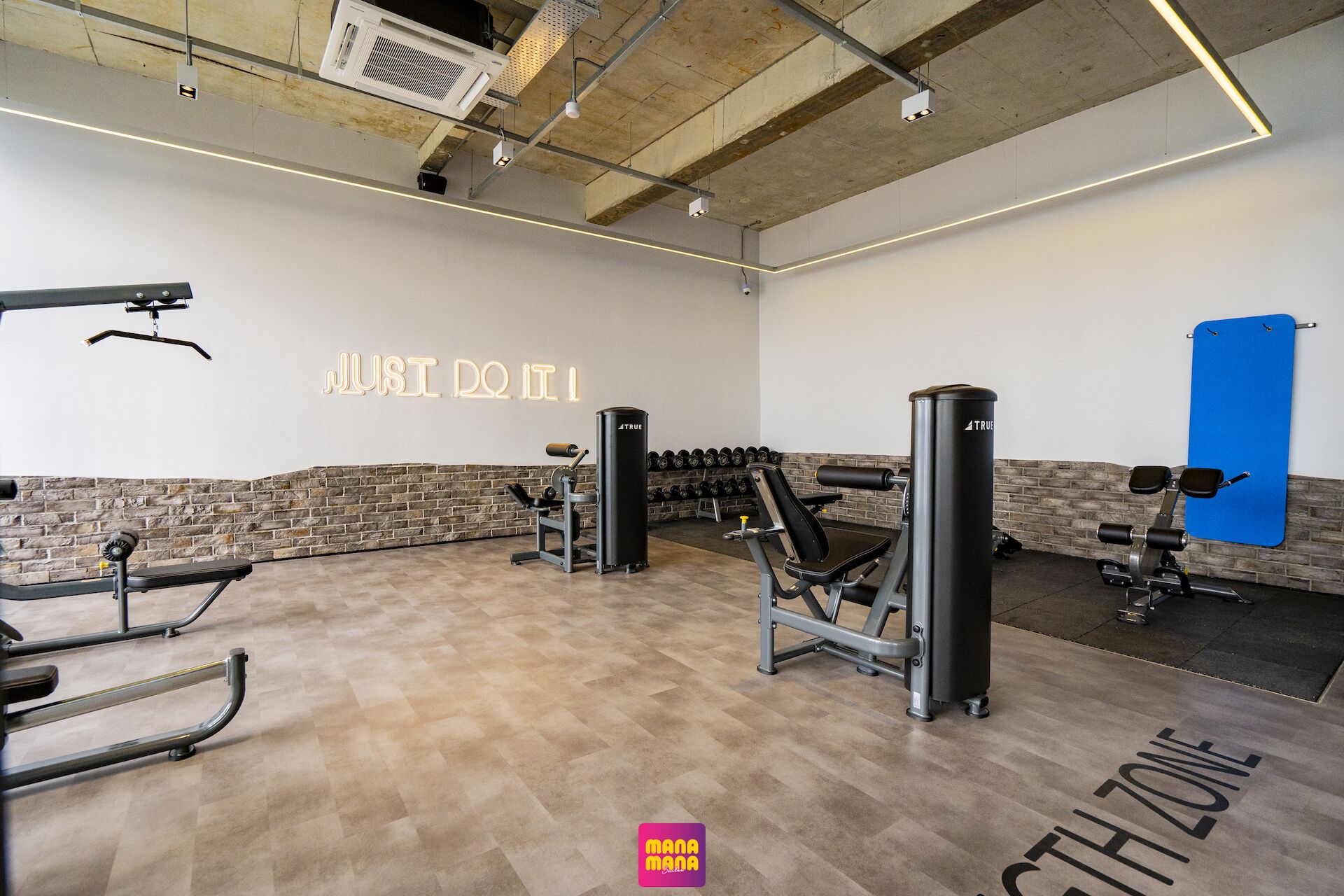 Un gimnasio con equipo de ejercicio, un mural motivacional y una colchoneta azul.