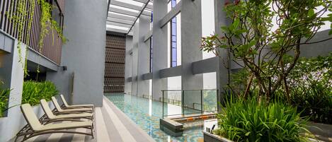 Una piscina interior con sillones de descanso, suelo de baldosas y vistas a la ciudad a través de amplios ventanales.