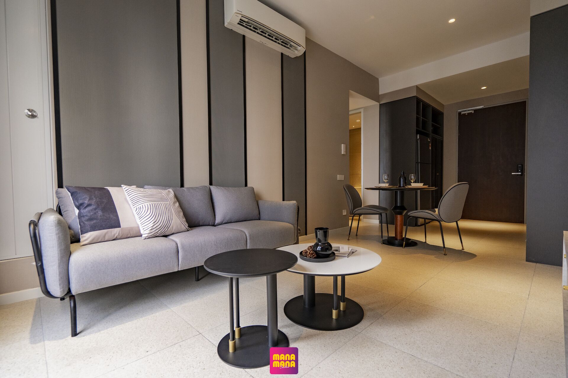 A modern living room with a grey sofa, two round tables, and a dining area with chairs.
