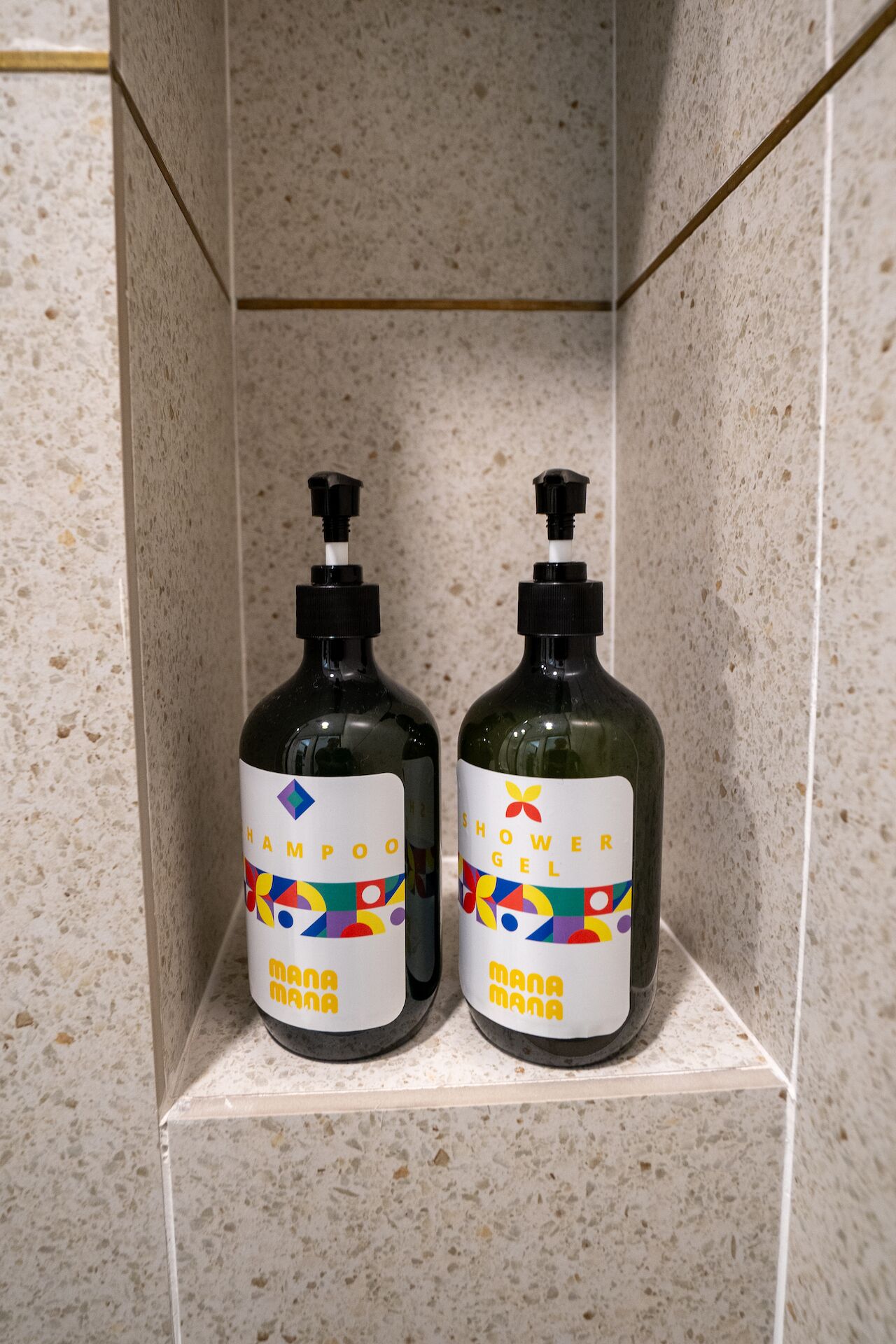 Deux bouteilles de shampoing et de gel douche sur une étagère carrelée dans la salle de bain.