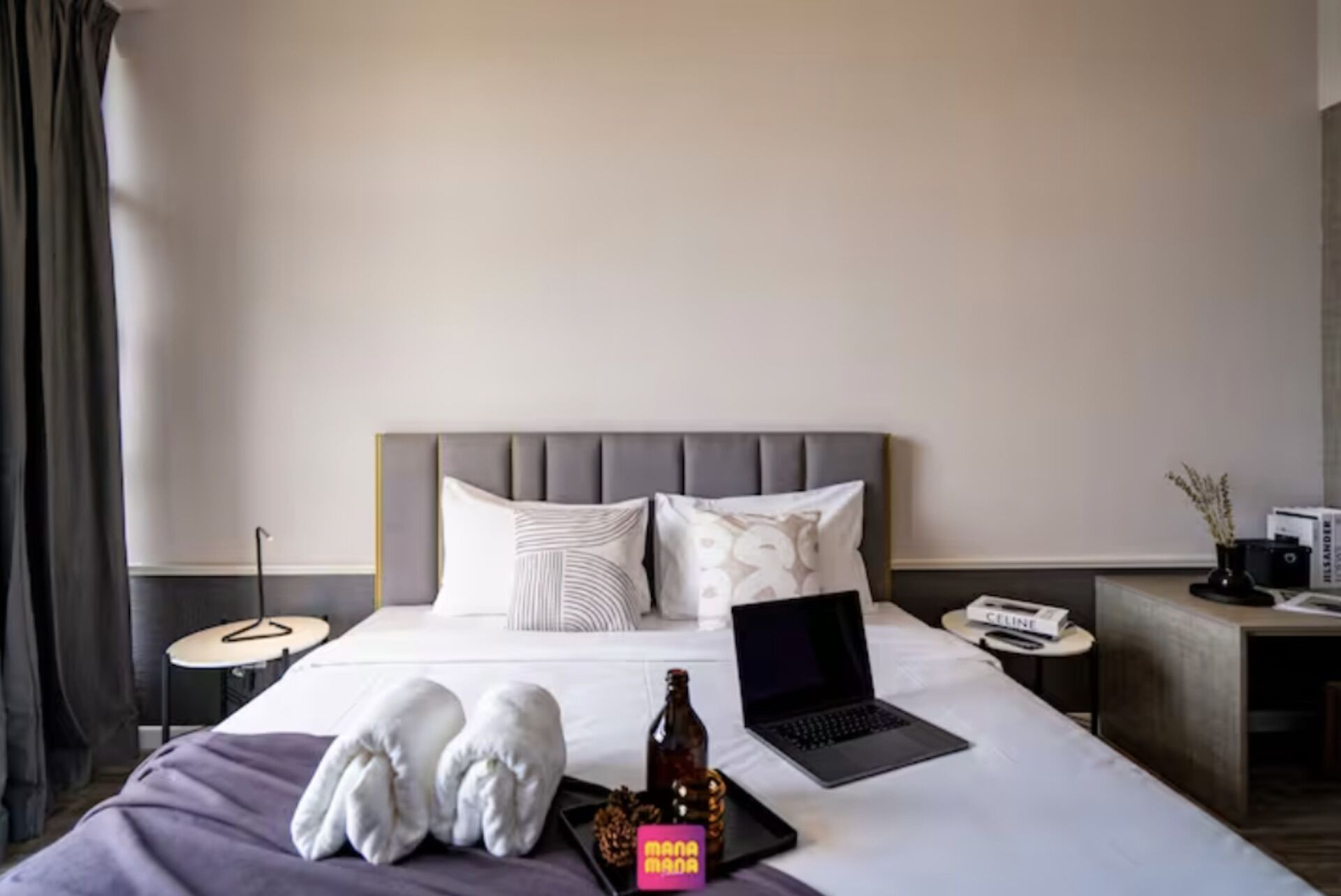 Ein ordentlich bezogenes Bett mit einem Laptop, einer Flasche und einer kleinen Schachtel mit dem Aufdruck "MANAMA".