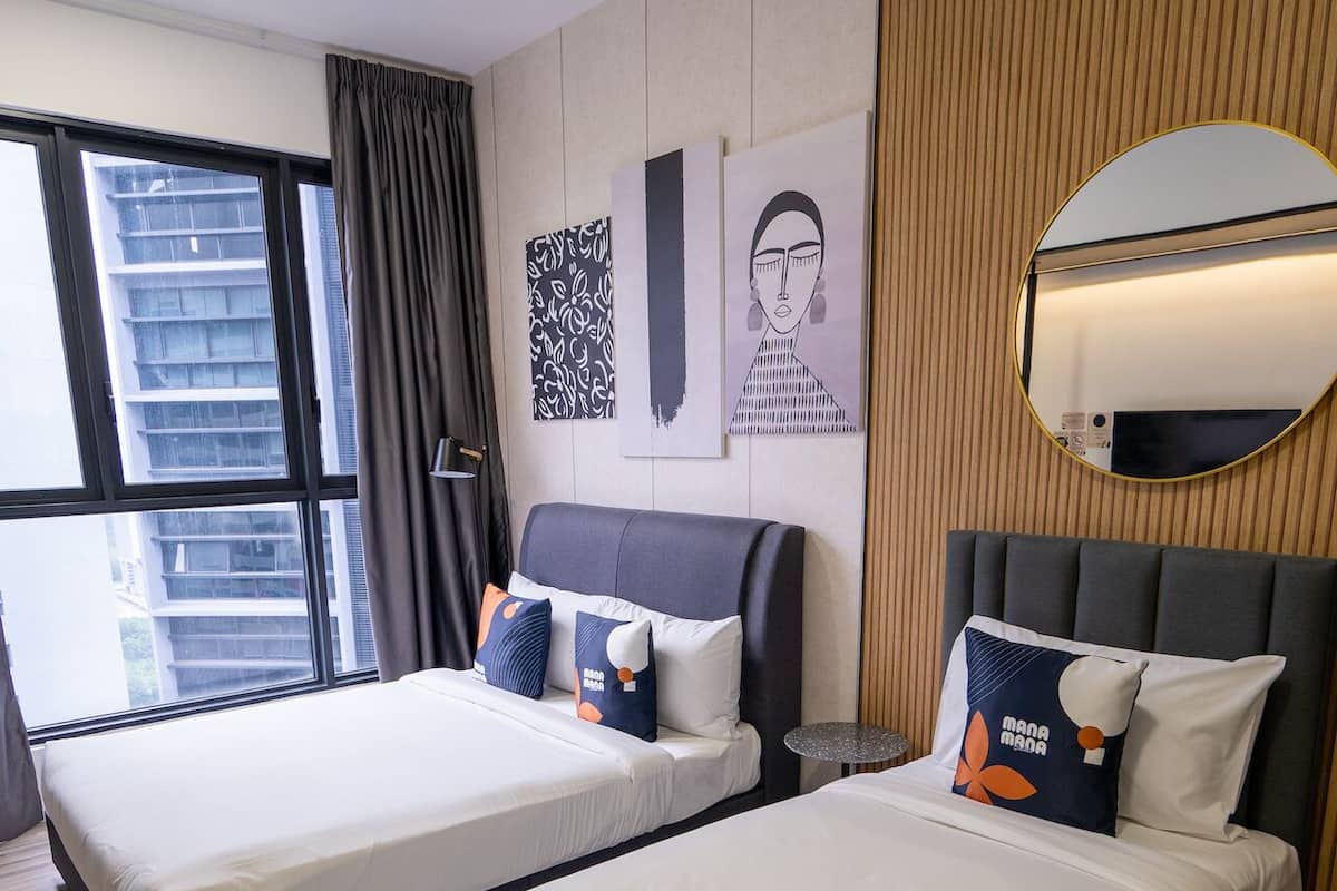 Habitación de hotel con dos camas, ventilador de techo, ventana grande y espejo en la pared.