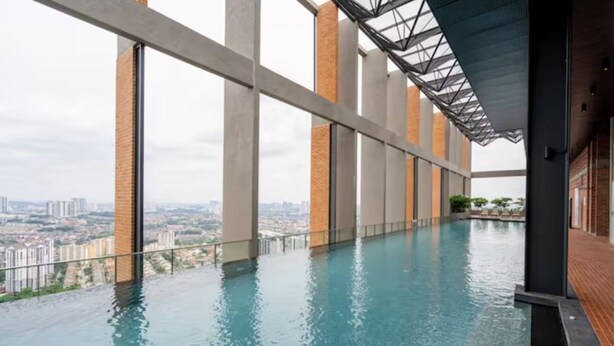 Une piscine à débordement intérieure offrant une vue sur la ville, entourée de grandes fenêtres et de piliers en béton.