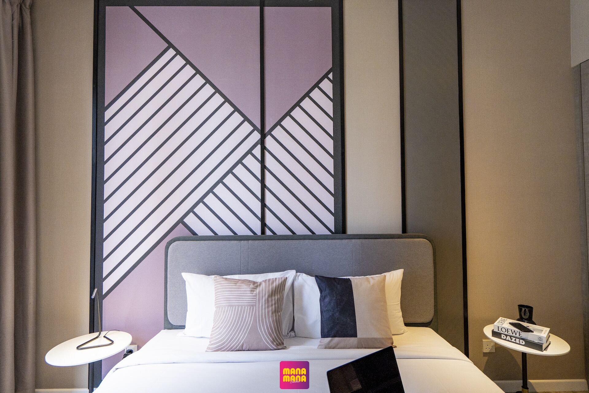 A hotel room with a bed, a headboard, a nightstand, a lamp, and a wall with a geometric pattern.