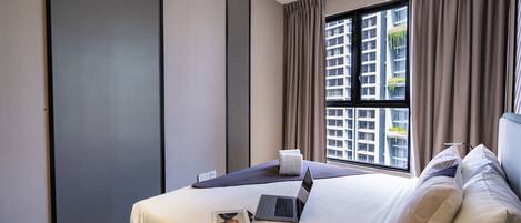 A modern hotel room with a large bed, a laptop, and a window with curtains.