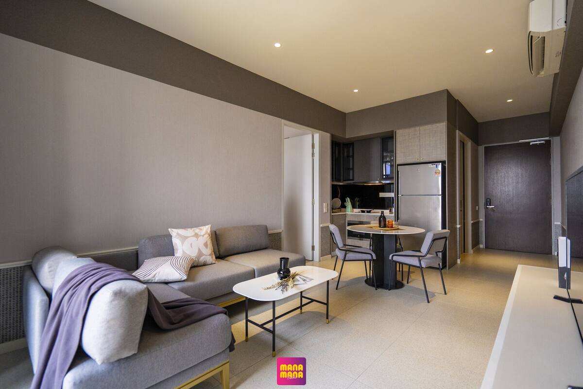 Una sala de estar moderna con un sofá gris, una mesita redonda y una cocina al fondo.