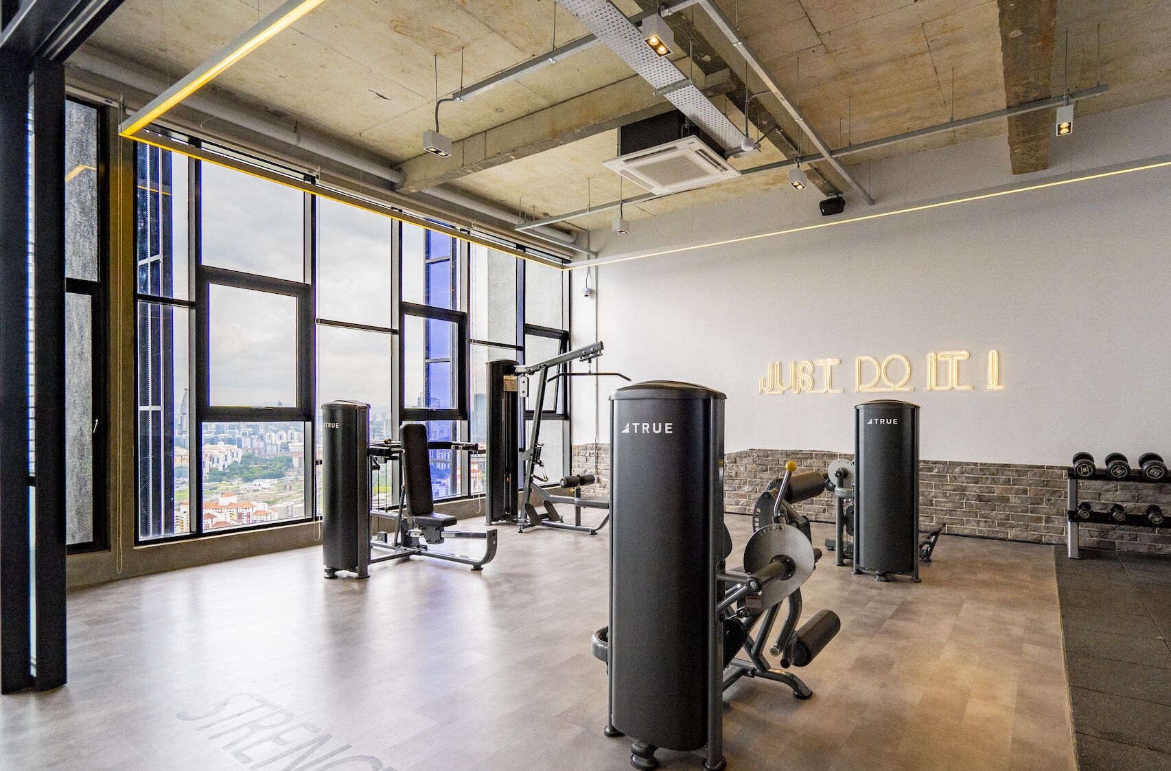 Une salle de sport équipée de matériel d’exercice, dotée de grandes fenêtres et ornée d’une affiche motivante au mur.