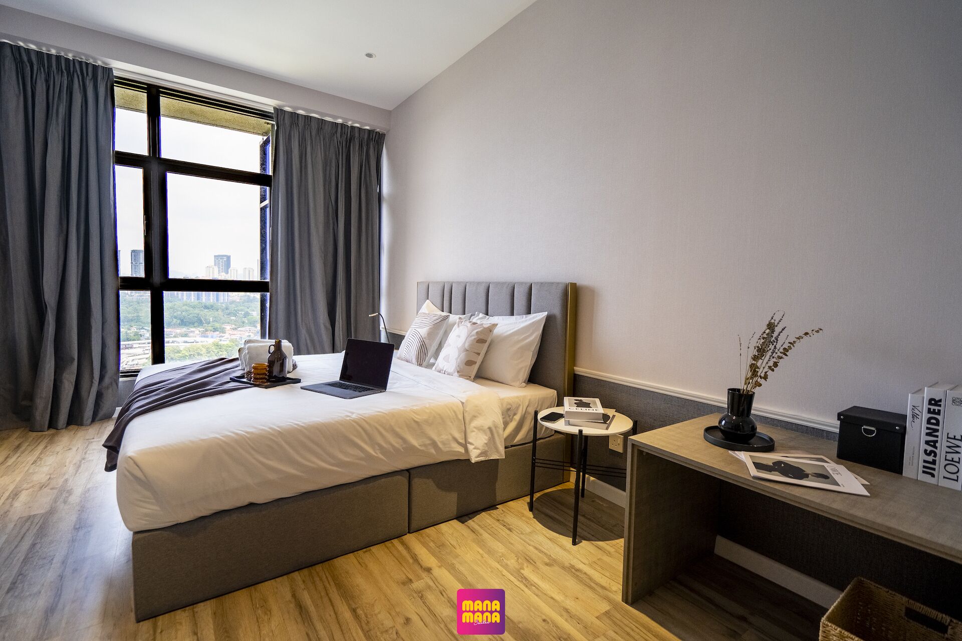 Een moderne hotelkamer met een groot bed, een nachtkastje met lamp, een klein bureau en stadszicht door grote ramen.
