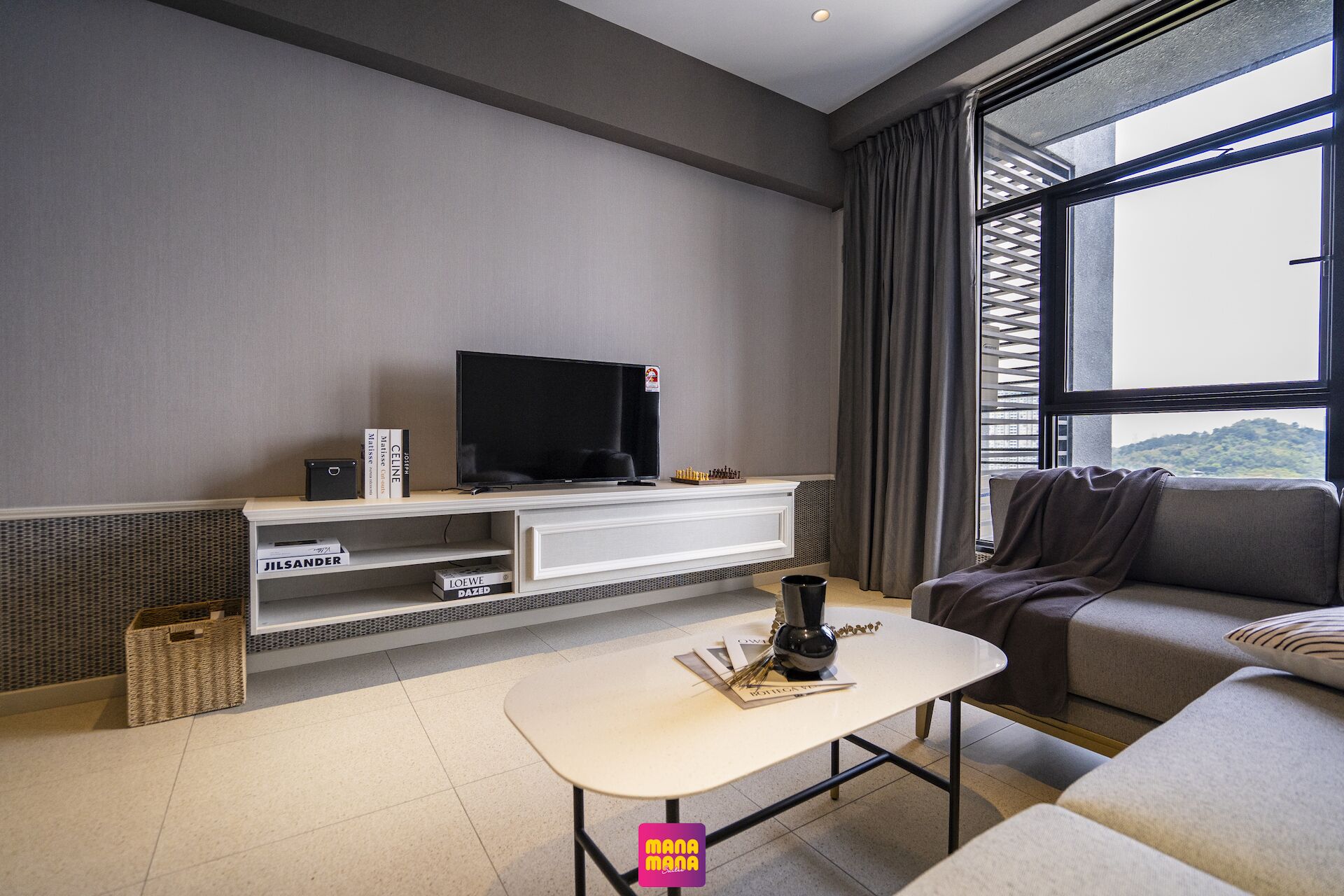 A modern living room with a flat-screen TV, a coffee table, a sofa, and a large window offering a view of the outdoors.